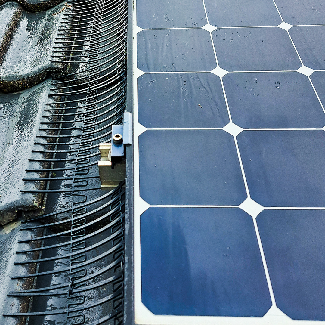 Close-up detailbeeld van vogelwering die netjes tussen dakpannen en zonnepanelen is geplaatst.